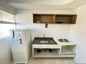 A compact kitchen with a white refrigerator, a granite countertop, a sink, and a wooden shelf above. - Lacqua DiRoma IV Via Caldas (Caldas Novas)
