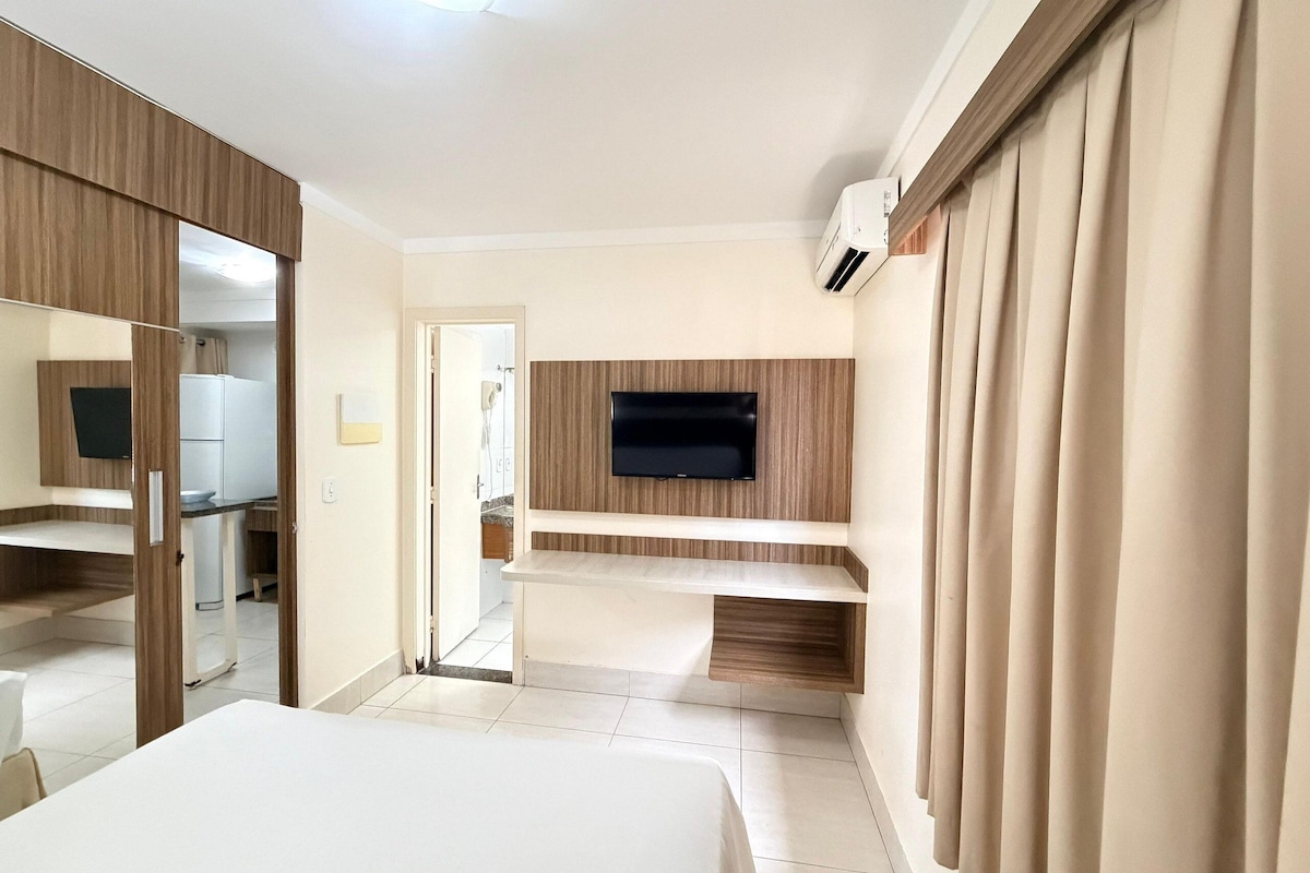 Habitación de hotel con cama, televisor montado en la pared, espejo y puerta que da a un baño.