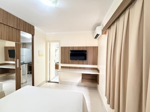 Habitación de hotel con cama, televisor montado en la pared, espejo y puerta que da a un baño.
