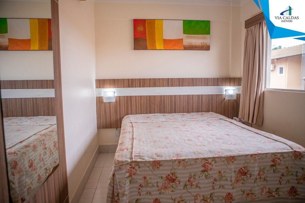 Habitación de hotel con cama, una obra de arte en la pared, ventana con cortinas y un logotipo visible.