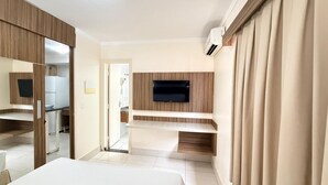 Habitación de hotel con cama, televisor montado en la pared, espejo y puerta que da a un baño.