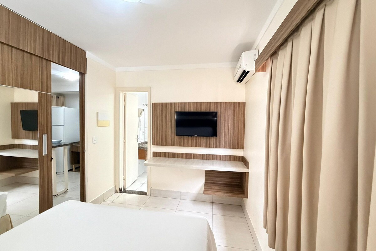 A hotel room with a bed, a TV mounted on the wall, a mirror, and a door leading to a bathroom.