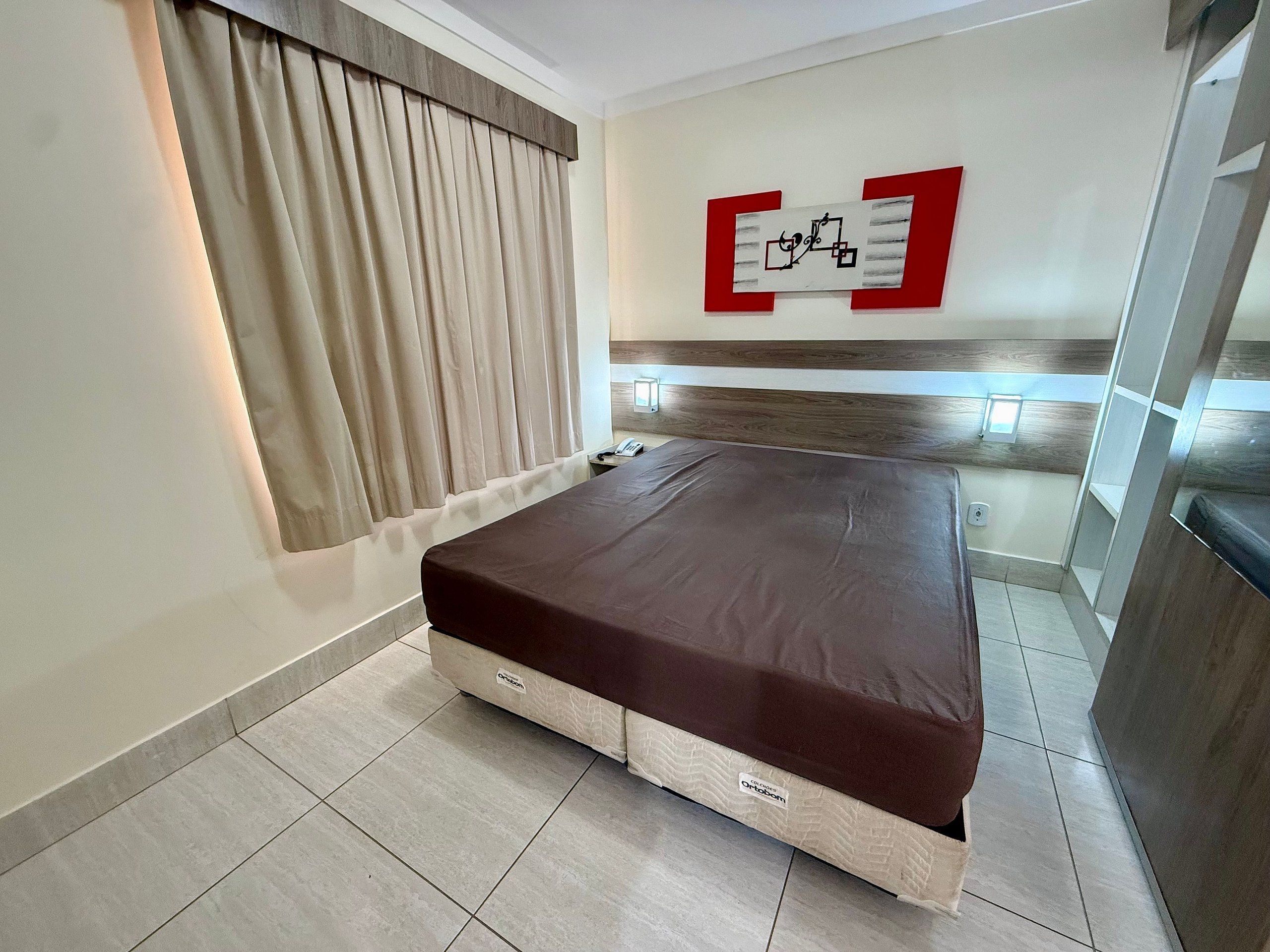 A bedroom with a bed, curtains, a wall-mounted artwork, and a bedside table.