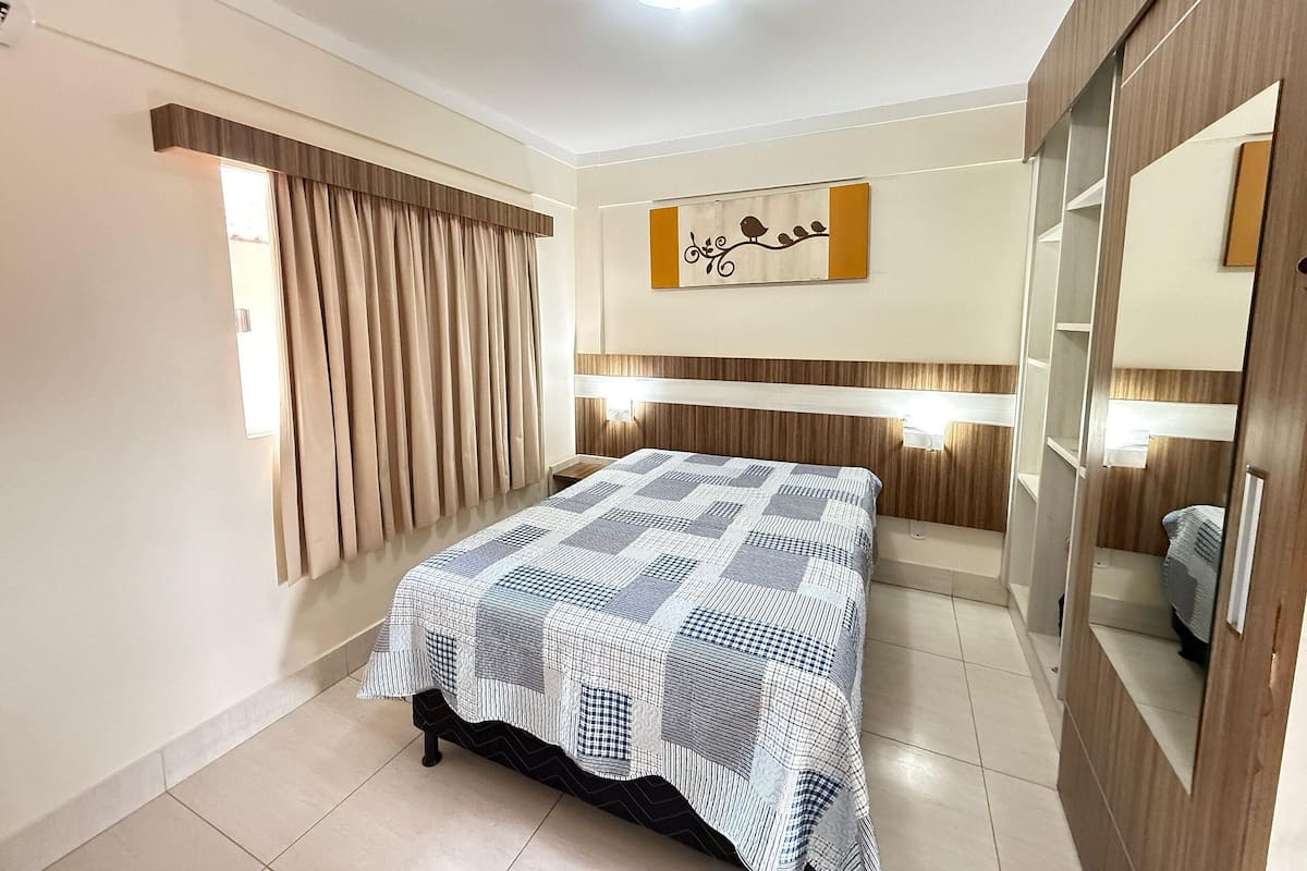 A bedroom with a bed, curtains, a wall-mounted artwork, a mirror, and a wardrobe.