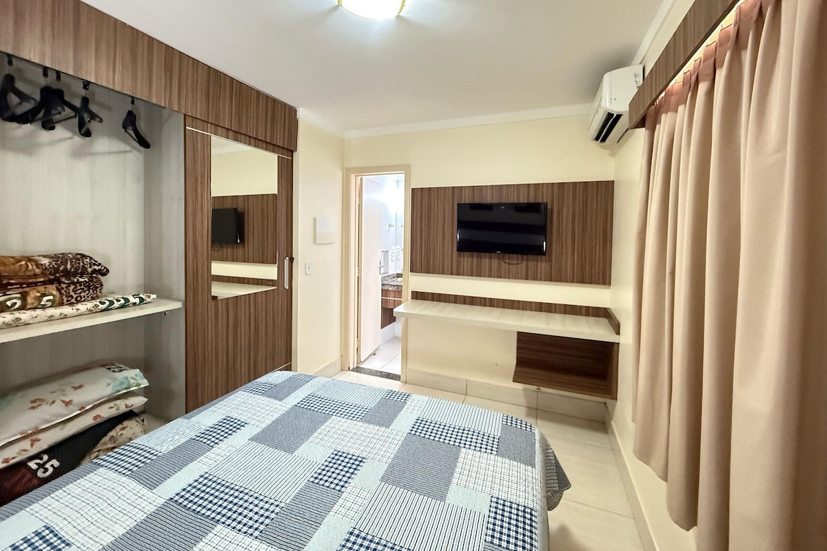 Un dormitorio con una cama, un televisor montado en la pared, un armario y un espejo.
