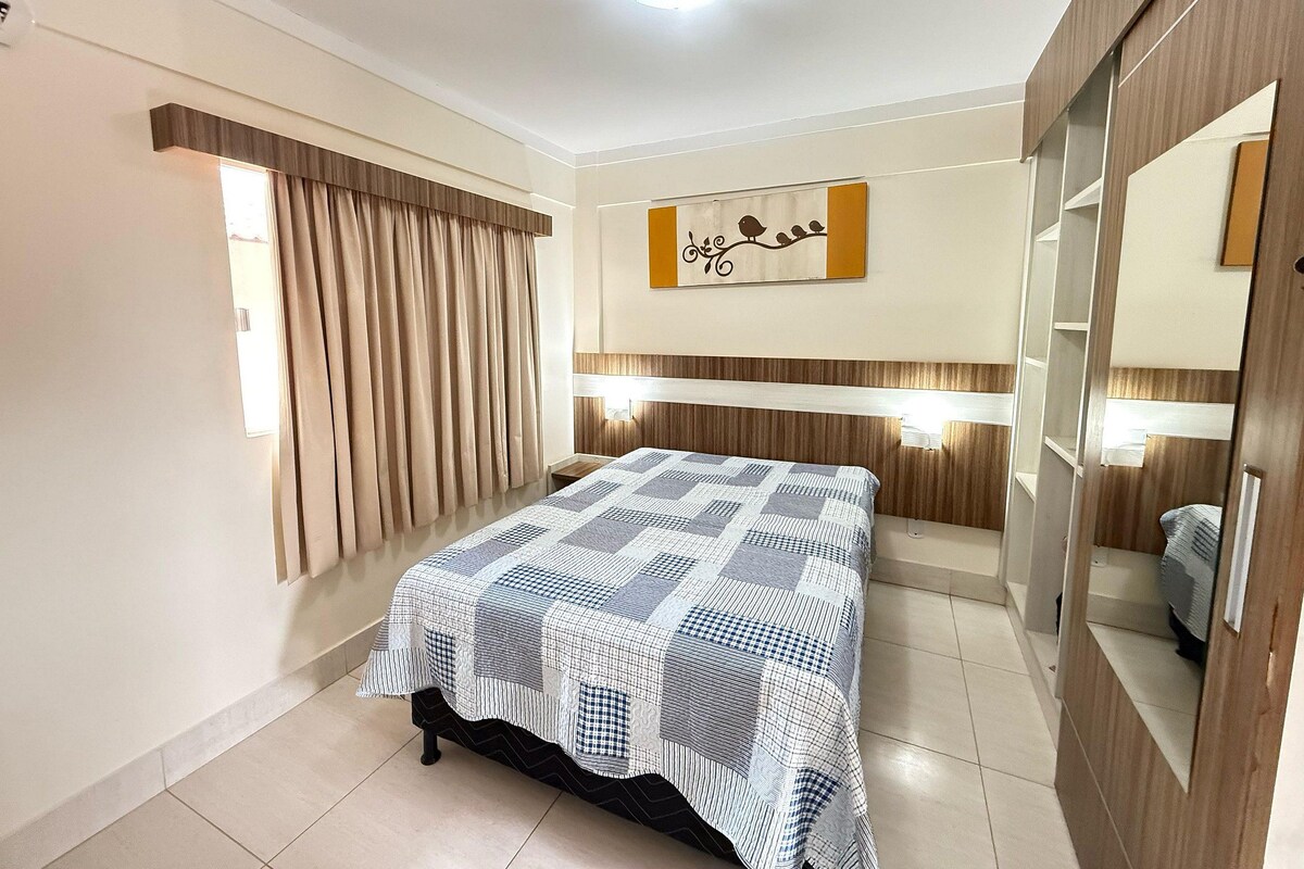 A bedroom with a bed, curtains, a wall-mounted artwork, a mirror, and a wardrobe.