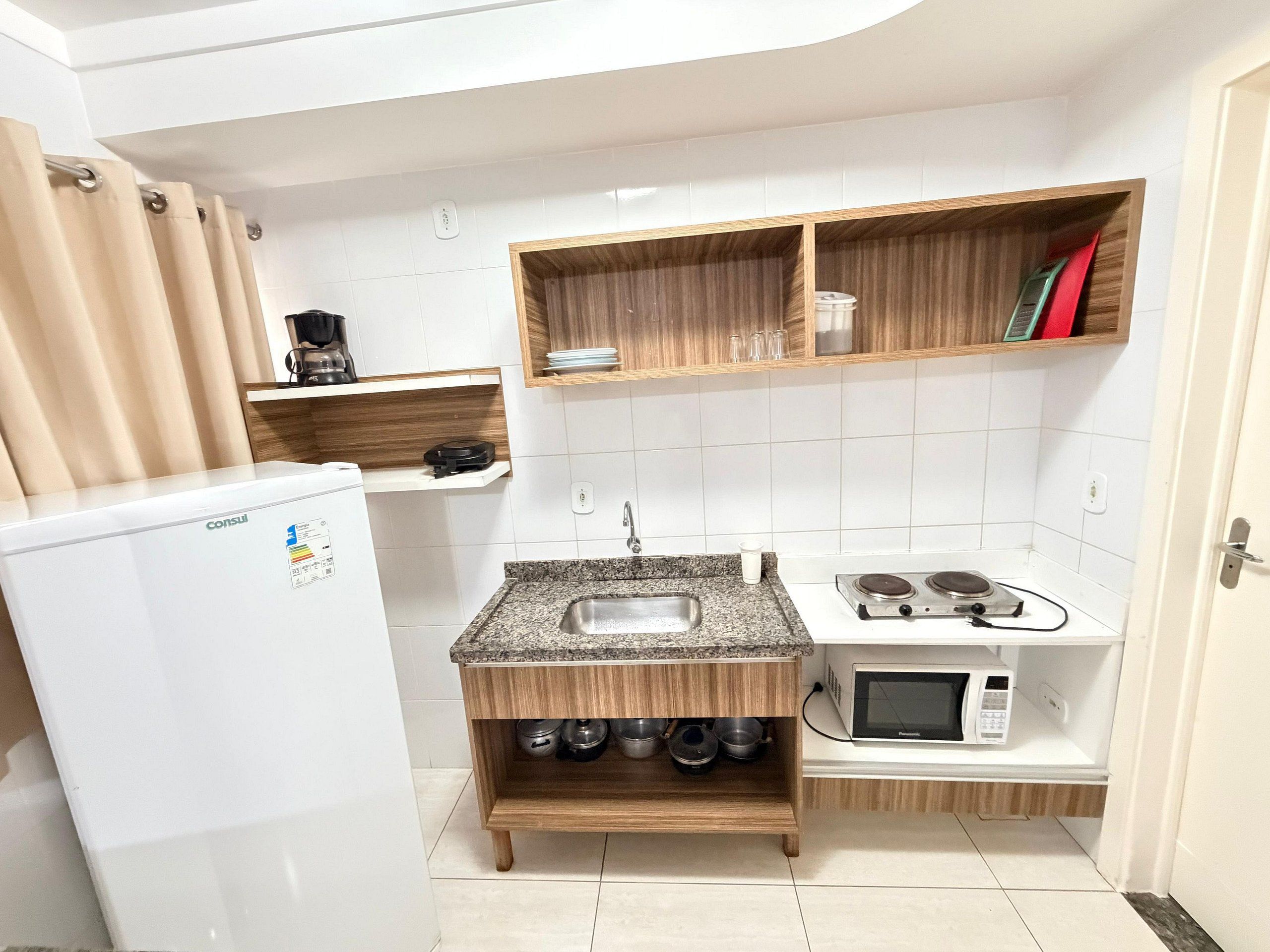 A compact kitchen with a refrigerator, a sink, a microwave, and wooden shelves.