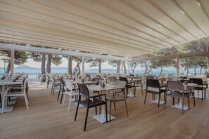 An outdoor dining area with tables and chairs arranged under a canopy, overlooking a scenic view of trees and mountains.