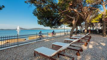 A beachside area with sun loungers, a fence, and a view of the sea.