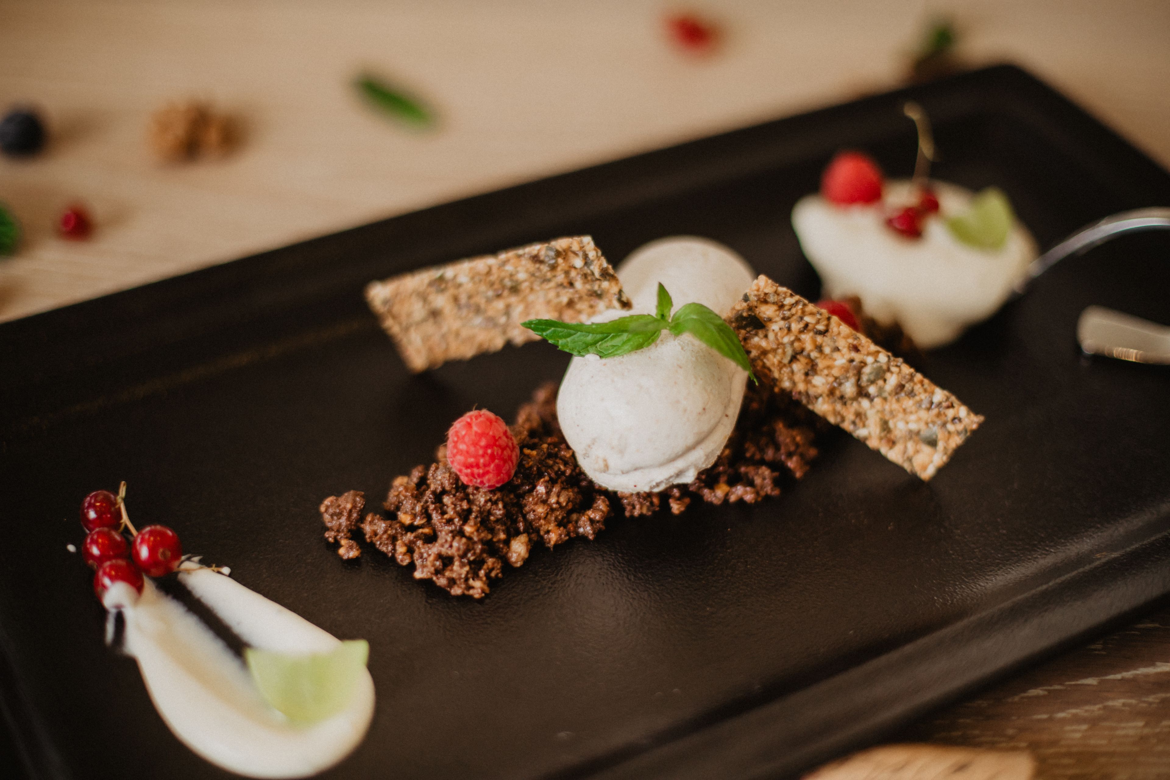 Un piatto dessert con una pallina di gelato, un lampone e una fetta di torta su un piatto nero.