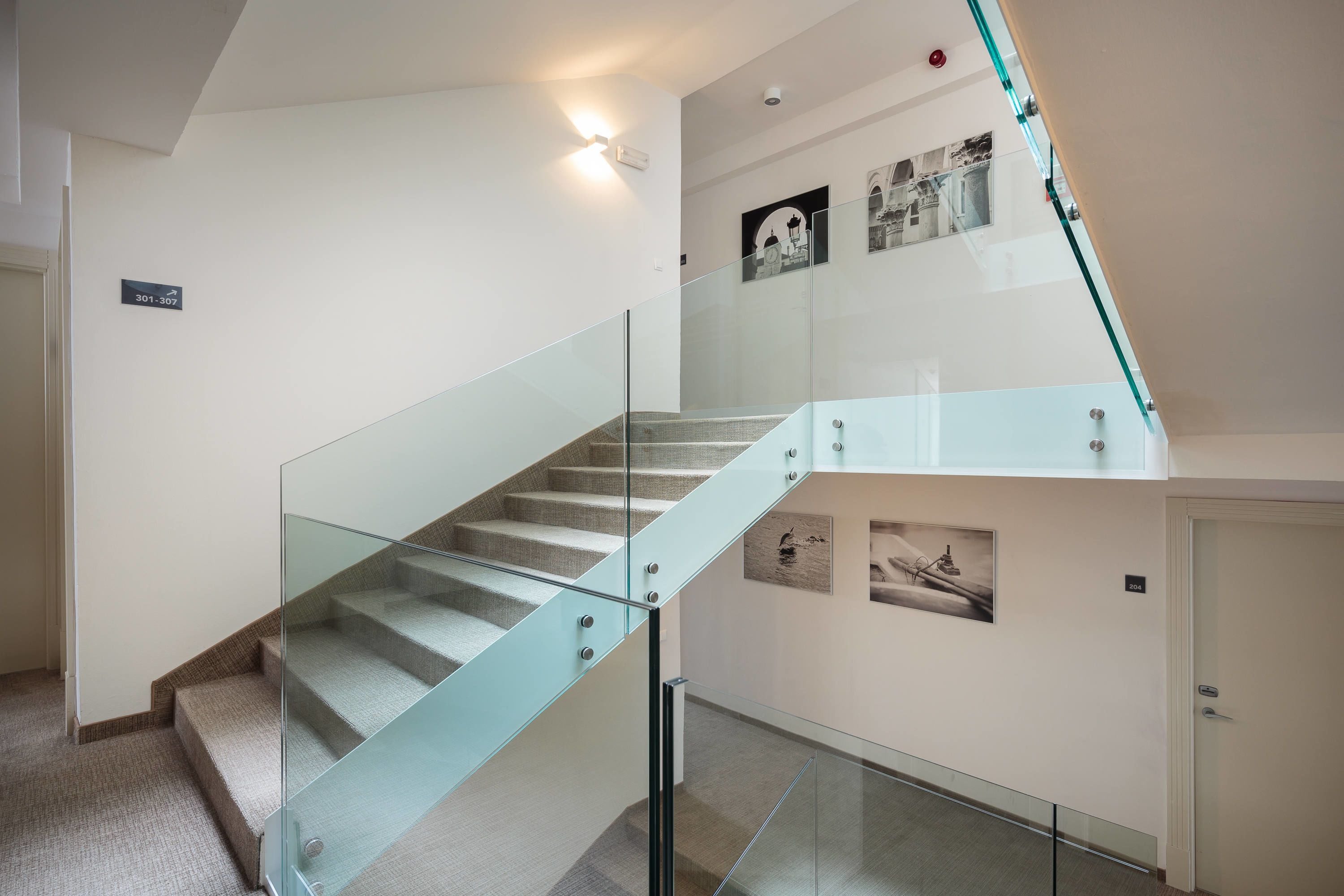 Een moderne trap met glazen balustrades, een vloerbedekking en wanddecoratie.