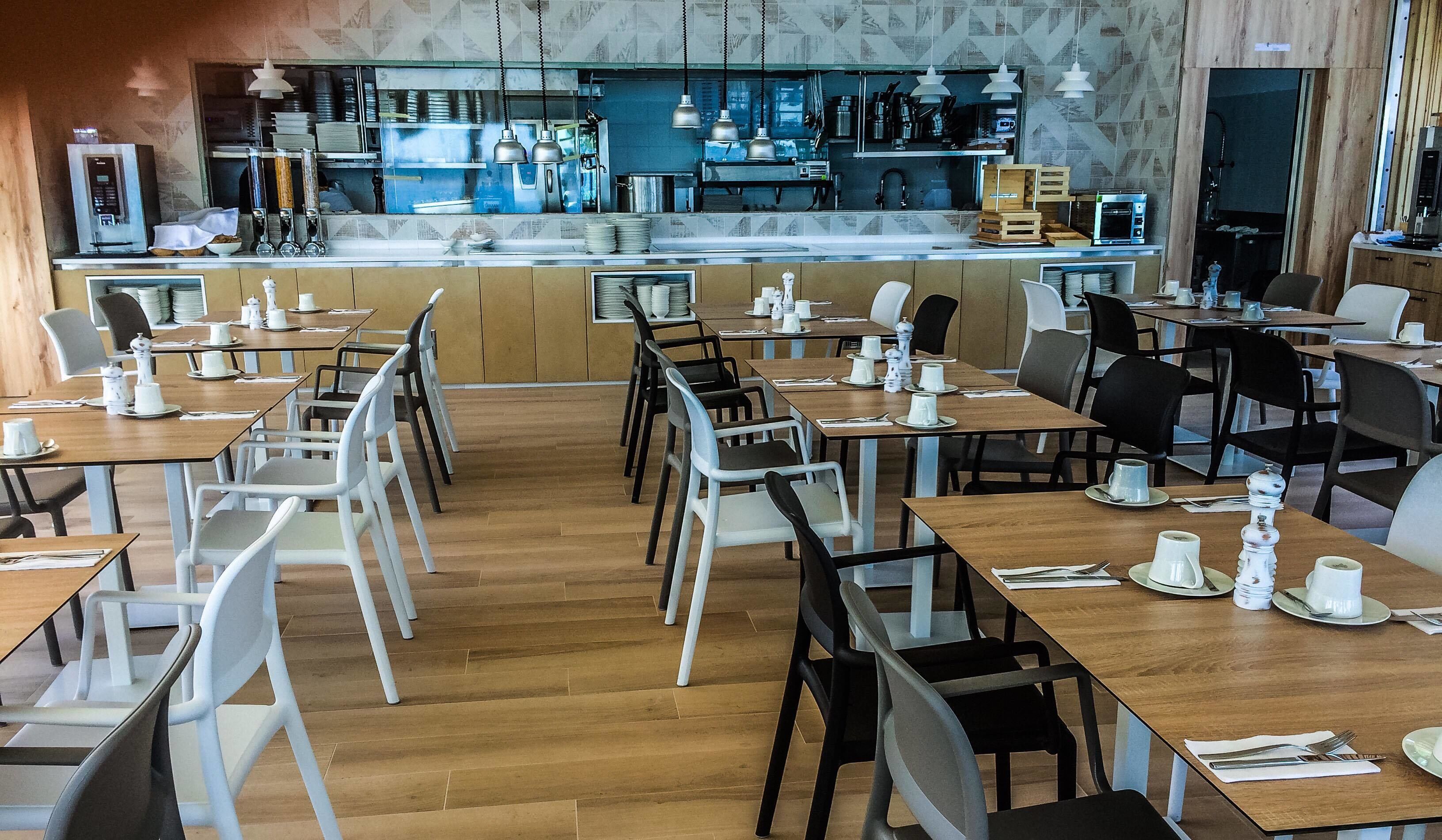 Un restaurante con mesas y sillas de madera, una zona de bar con equipo de cocina y un salpicadero de azulejos.