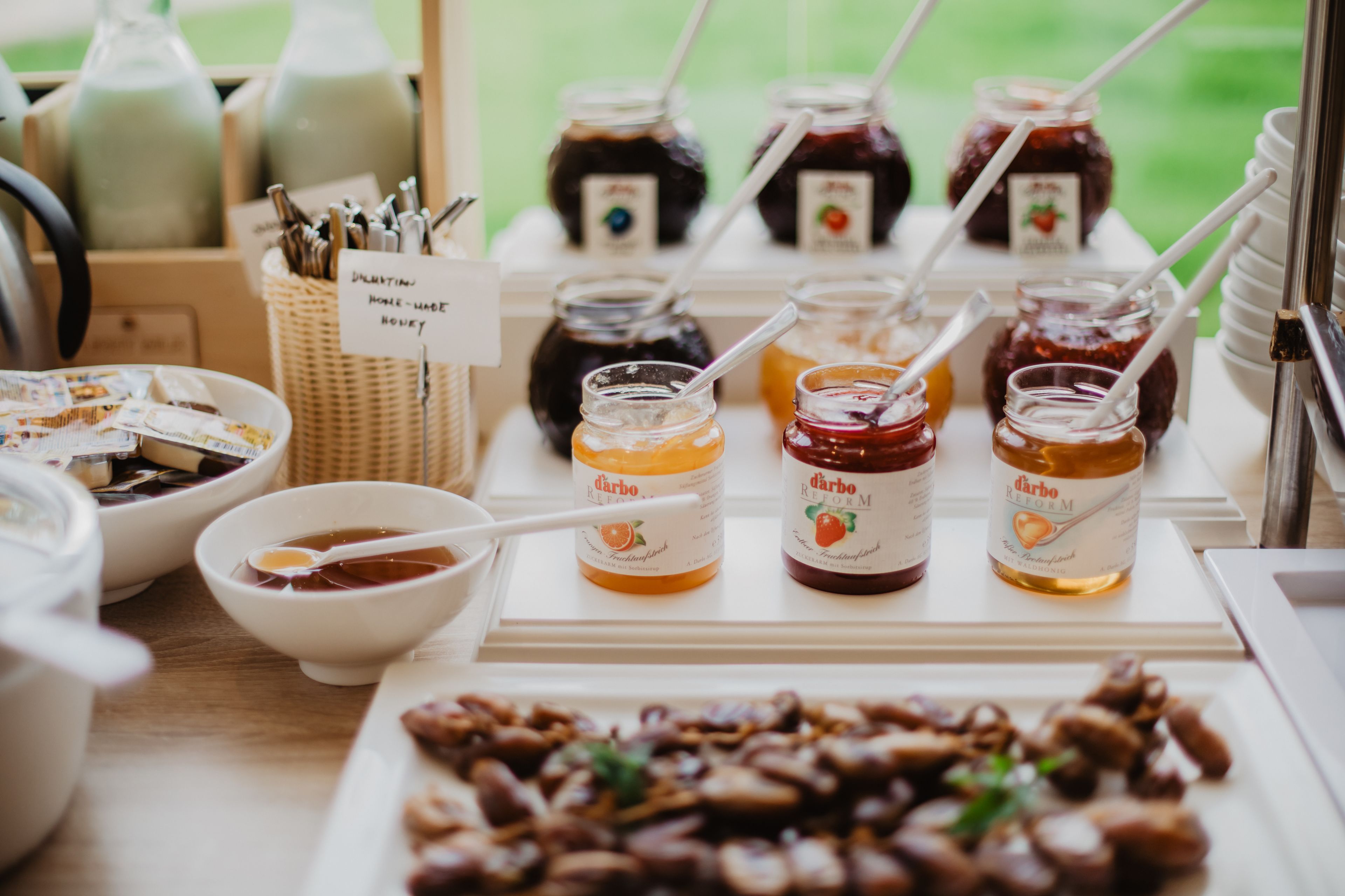 A buffet table with various jars of jam and honey, bowls of soup, and a plate of nuts.