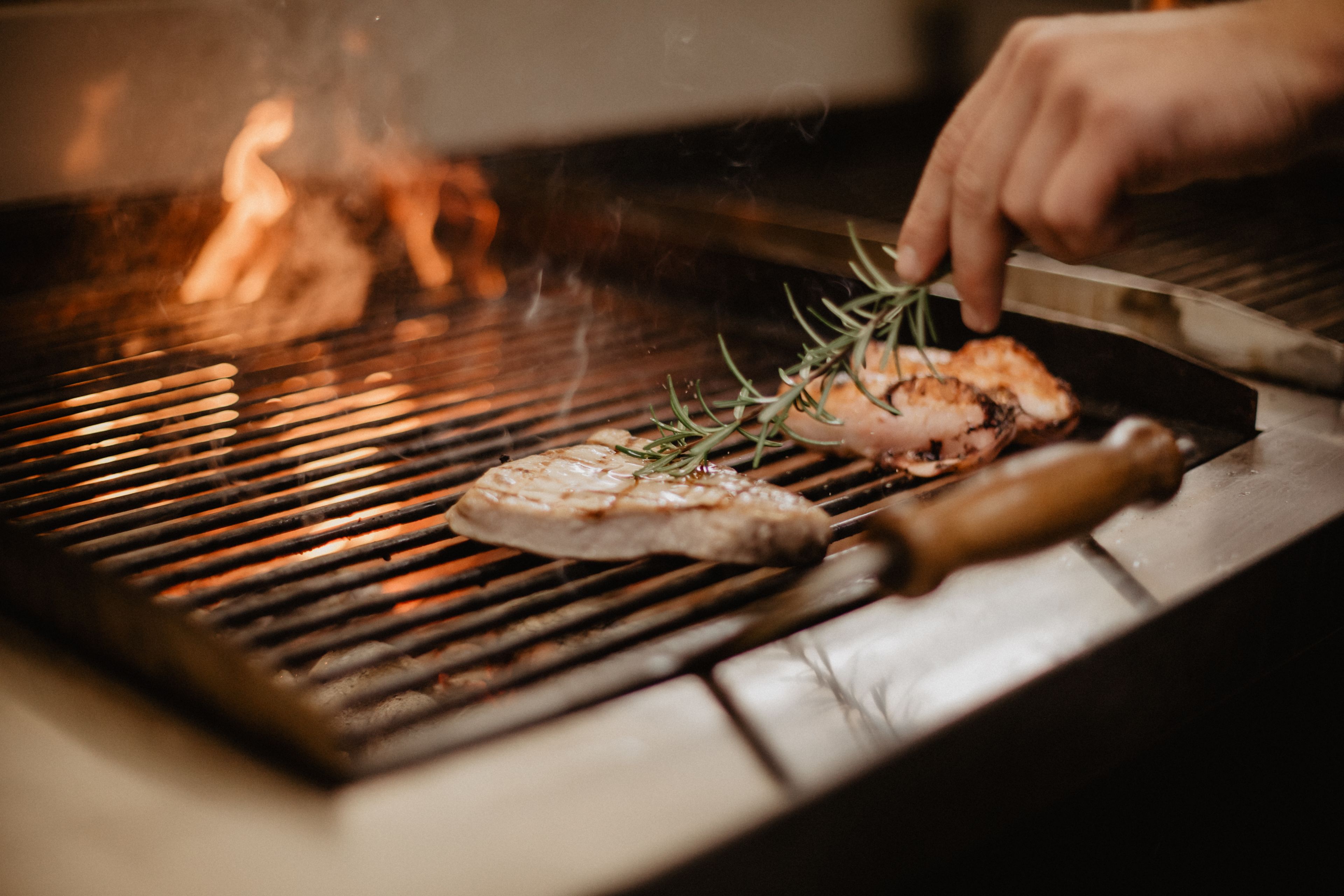 A steak being grilled on a grill with a hand holding a knife.