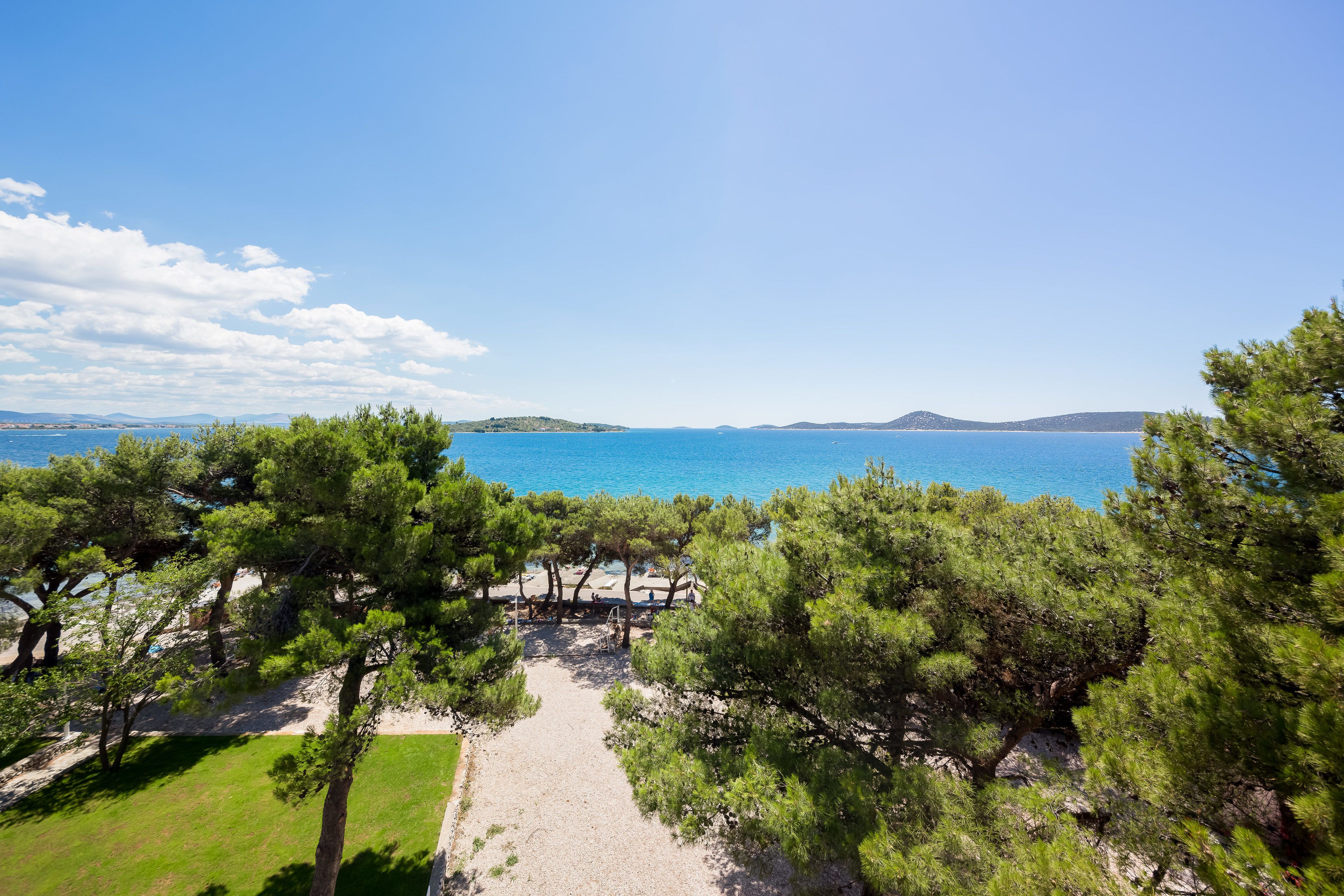 A coastal path leading to a beach area with trees and a clear view of the sea.