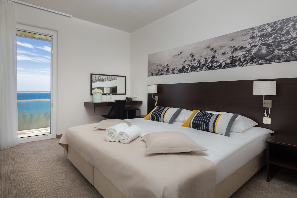 Habitación de hotel con una cama grande, un escritorio, una silla, una mesita de noche, una lámpara de pared y vistas al océano.