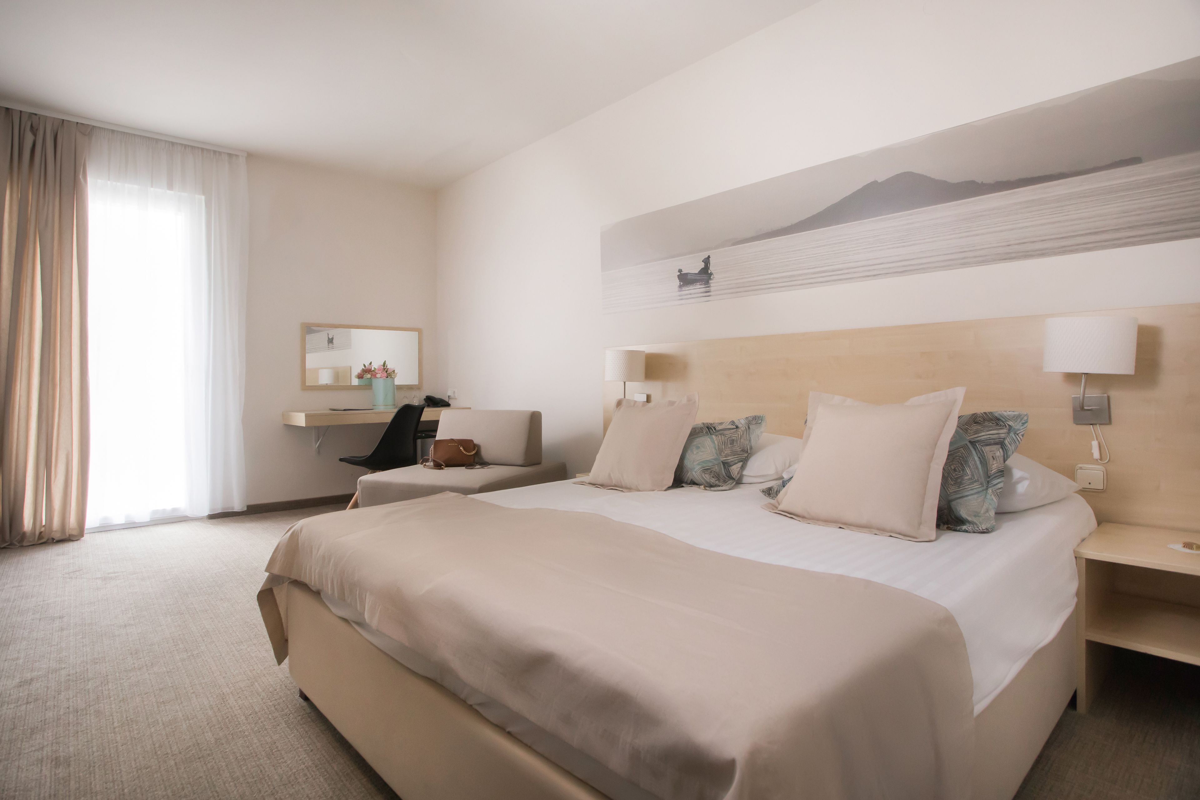 Una habitación de hotel con una cama grande, un escritorio, una silla y un ventanal con cortinas.