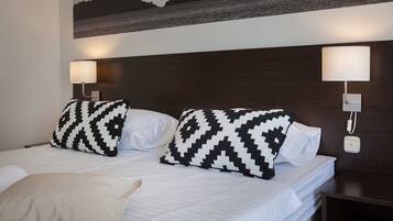 A hotel room with a bed, two patterned pillows, a bedside lamp, and a wall-mounted phone.