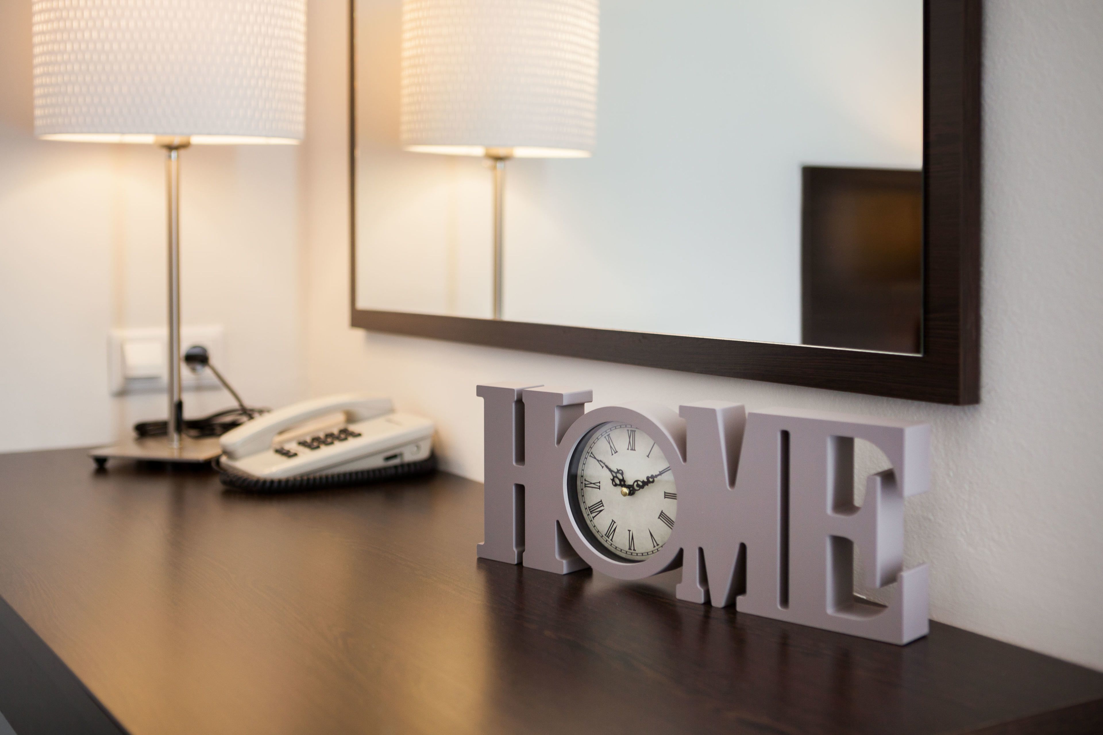 A wooden desk with a clock and a lamp, a mirror, and a 'HOME' sign.