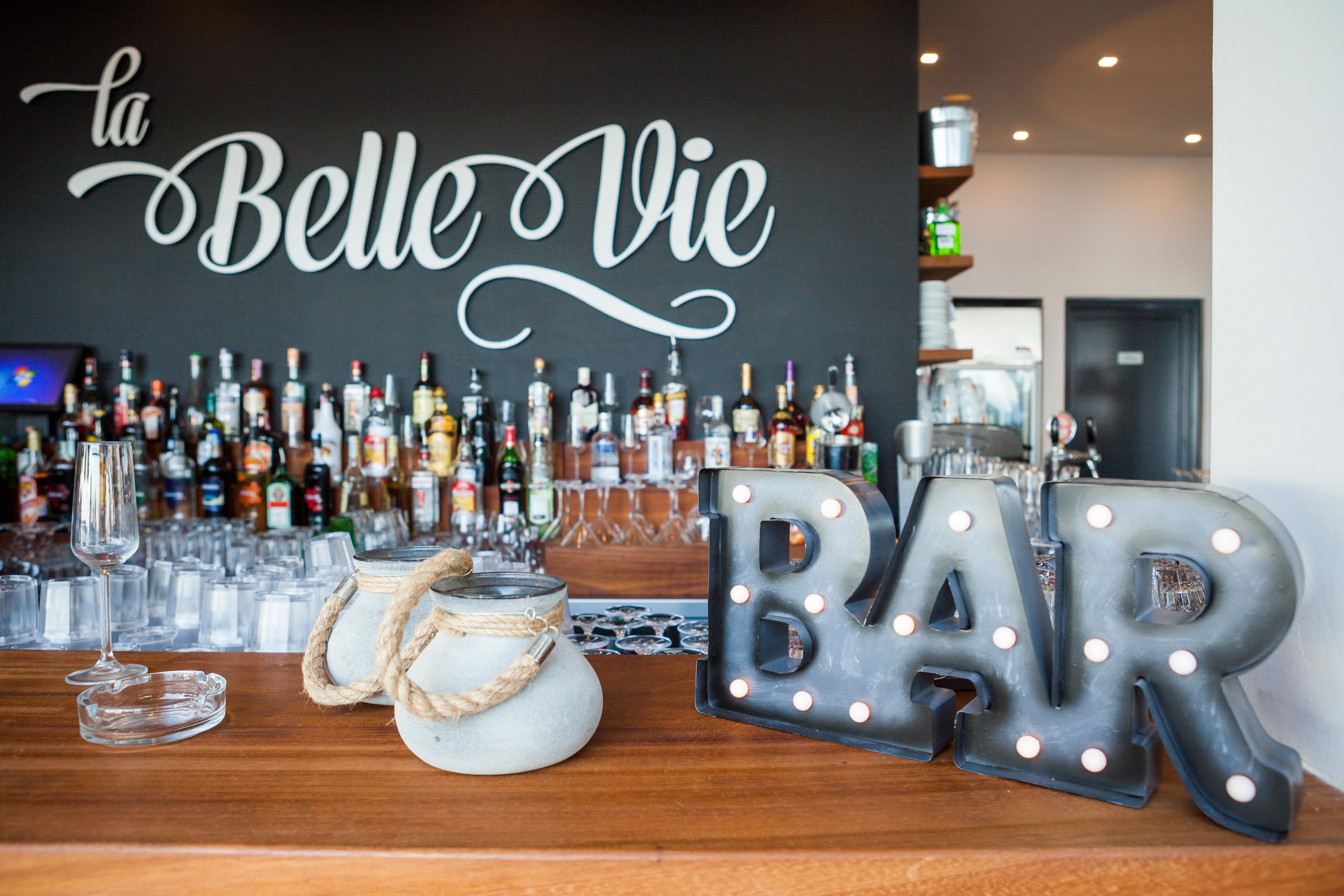 A bar area with a sign reading "la Belle Vie" and illuminated letters spelling "BAR".