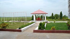 Un kiosque doté d’un toit à rayures rouges et blanches, entouré d’une pelouse bien entretenue et de parterres de fleurs, avec une aire de jeux en arrière-plan.