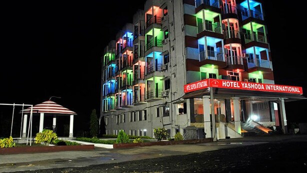 Un hôtel à plusieurs étages doté de balcons, d’une enseigne rouge indiquant qu’il s’agit d’un hôtel, et d’une zone couverte avec un toit à rayures.