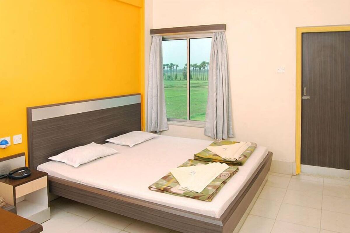 Une chambre d’hôtel avec un lit, une fenêtre avec des rideaux, une porte et une petite table avec un téléphone.