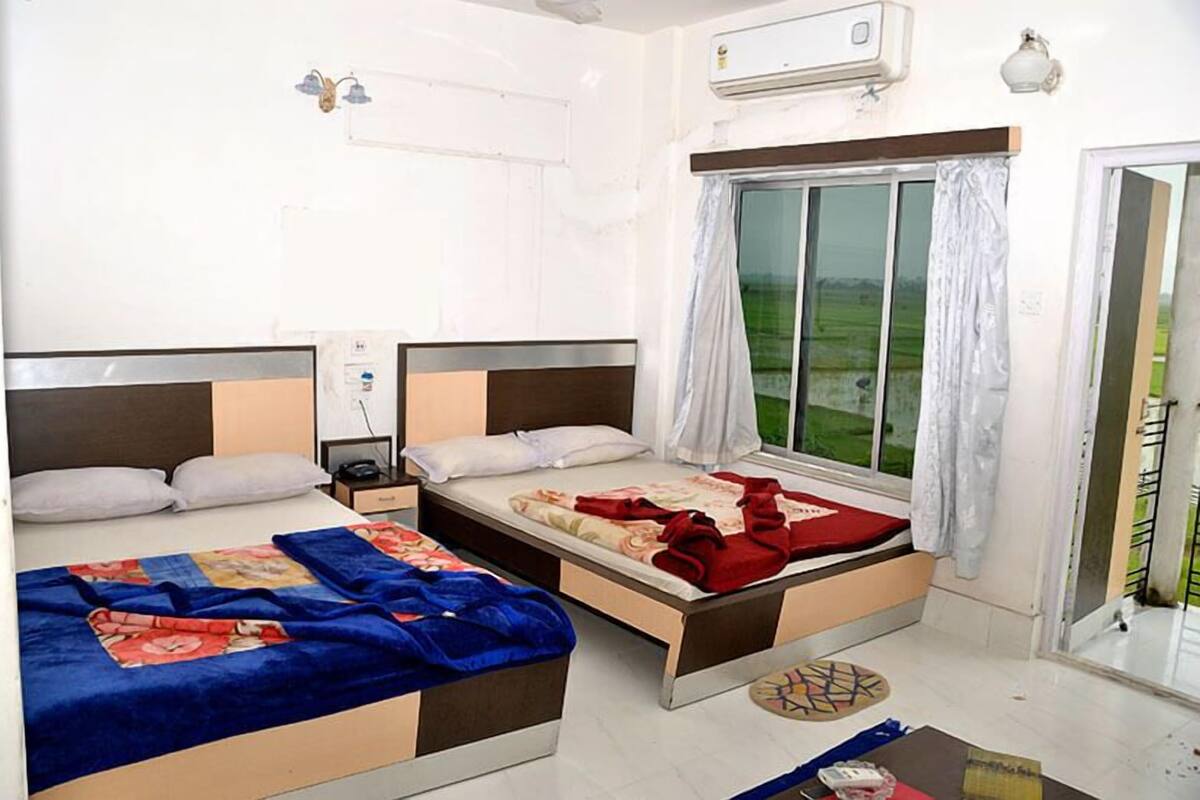 Une chambre d’hôtel avec deux lits, une fenêtre avec des rideaux, un appareil de climatisation et une table de chevet.