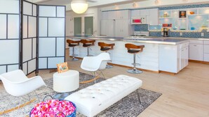 A modern kitchen with a central island, bar stools, and a dining area with white chairs. - Nestled in the Cove (Rancho Mirage)