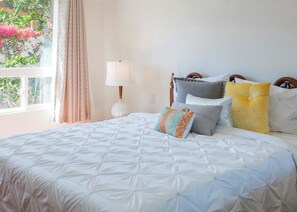 A neatly made bed with a white quilt, a bedside lamp, and several pillows in various colors. - Nestled in the Cove (Rancho Mirage)
