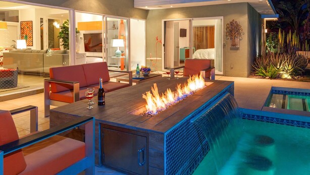 An outdoor living area with a fire feature, seating, and a pool. - Nestled in the Cove (Rancho Mirage)