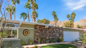 A modern house with a stone wall, palm trees, and a well-maintained lawn. - Nestled in the Cove (Rancho Mirage)