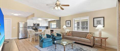 A modern living room with a sofa, two armchairs, a coffee table, and a kitchen in the background.