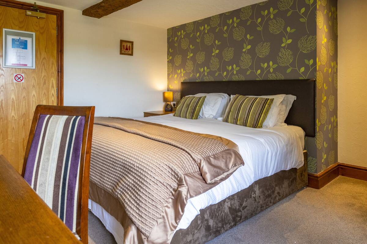 A bedroom with a large bed, a wooden headboard, a bedside table with a lamp, and a framed picture on the wall.