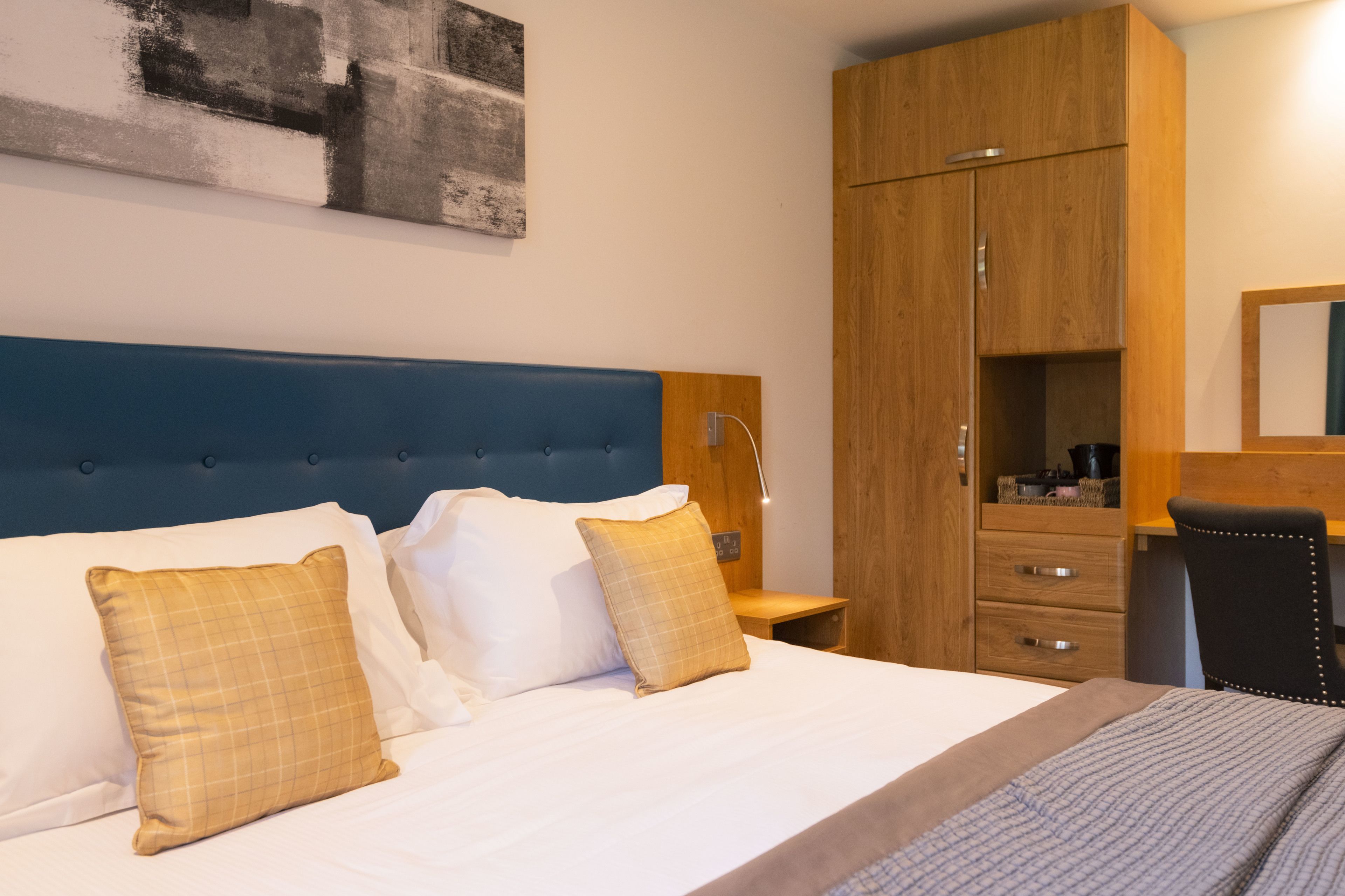 A hotel room with a large bed, a wooden wardrobe, a desk, and a chair.