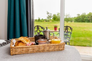 A wicker tray with breakfast items on a table by a window overlooking a garden. - The Stratford Park Hotel & Golf Club (Stratford-upon-Avon)