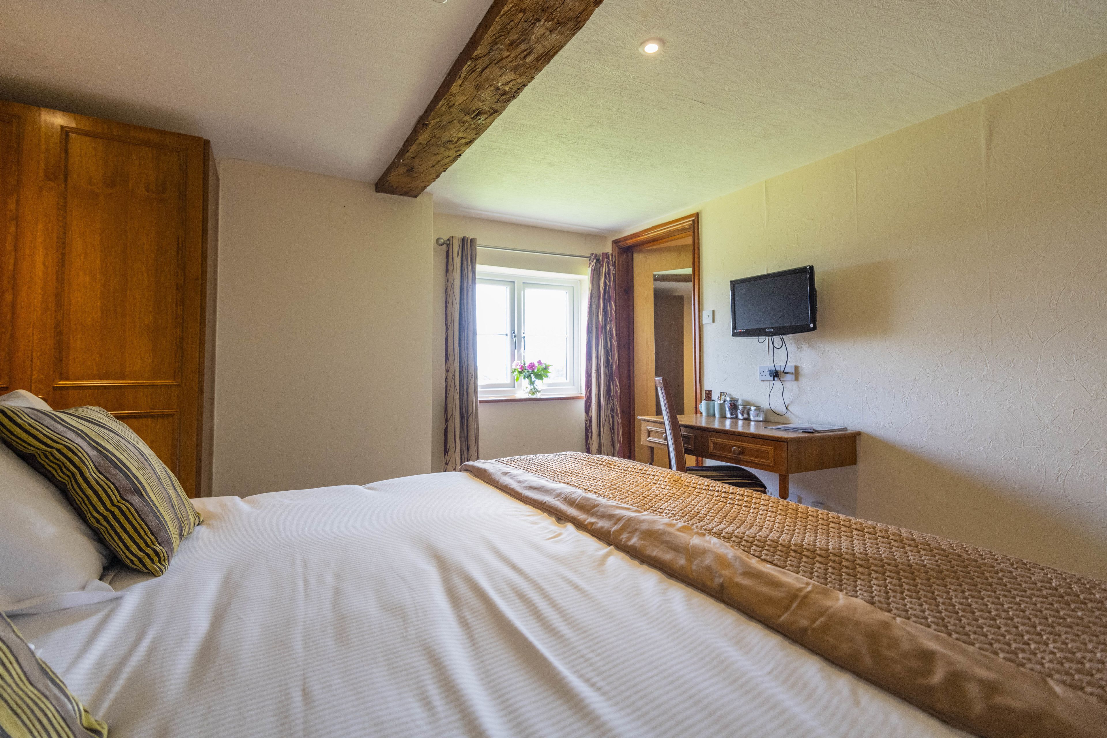 A bedroom with a bed, wooden wardrobe, desk, chair, and a TV mounted on the wall.