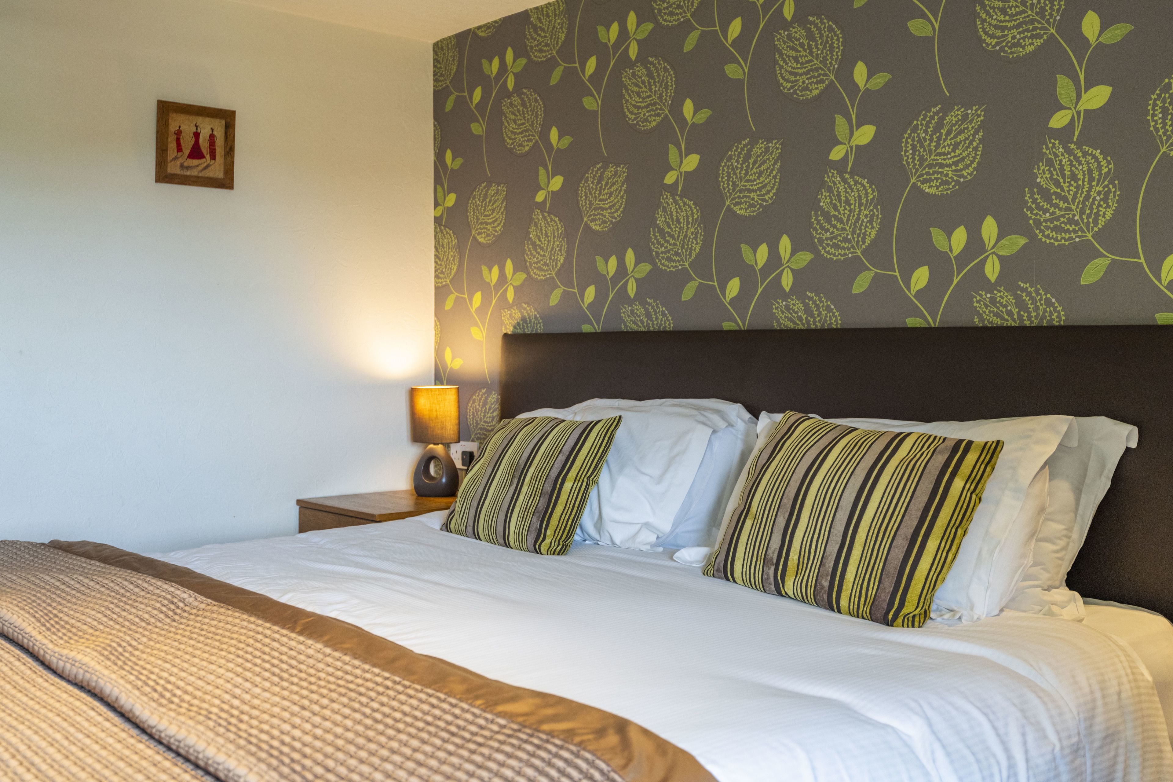 A hotel room with a bed, a nightstand, a lamp, and a floral-patterned wall.