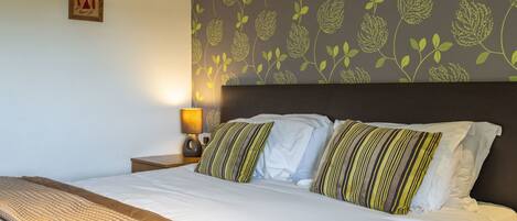 A hotel room with a bed, a nightstand, a lamp, and a floral-patterned wall.