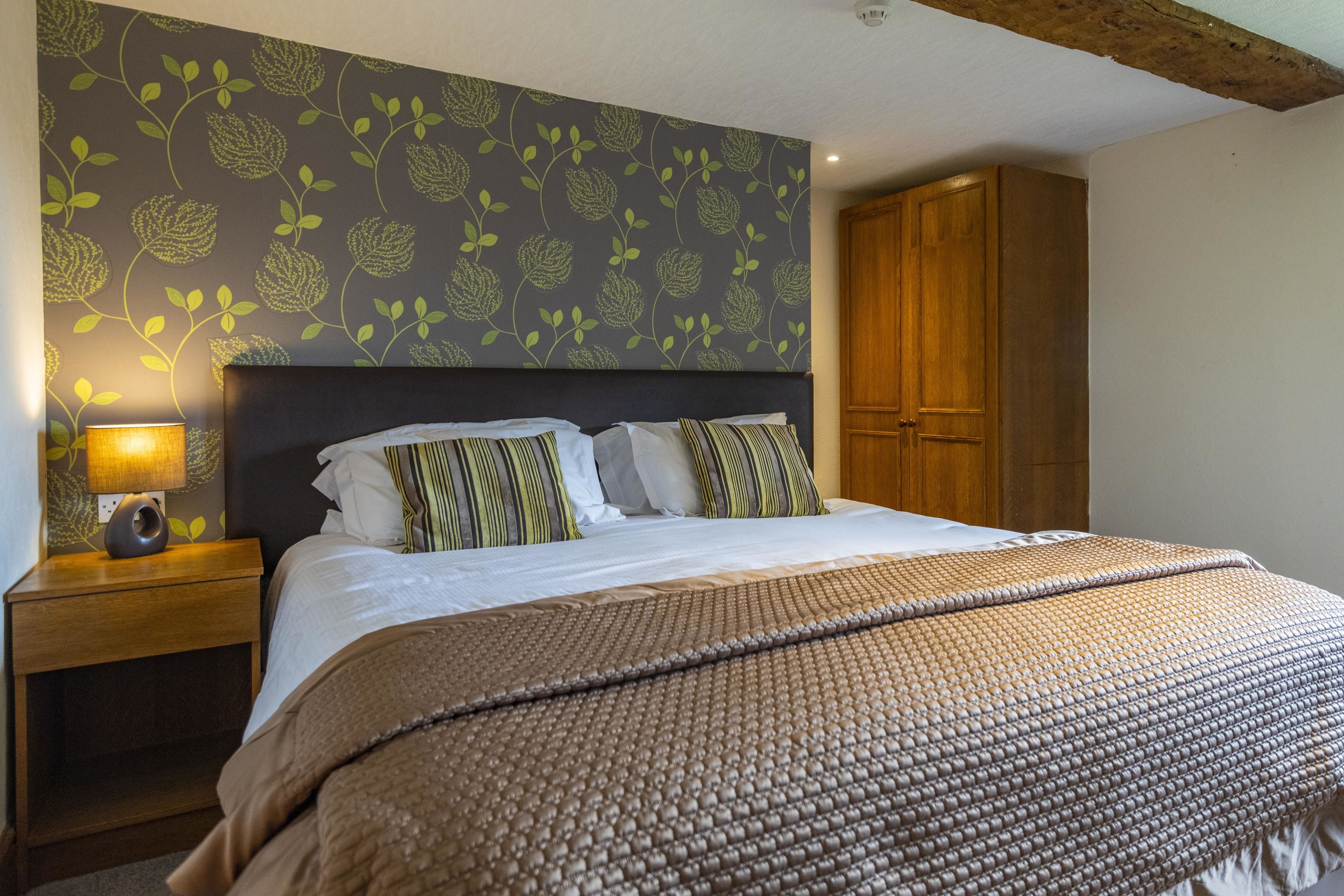 A neatly made bed with a patterned headboard, a wooden wardrobe, and a nightstand with a lamp.