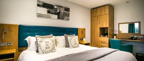 Una habitación de hotel moderna con una cama grande, un armario de madera, un escritorio y un espejo.