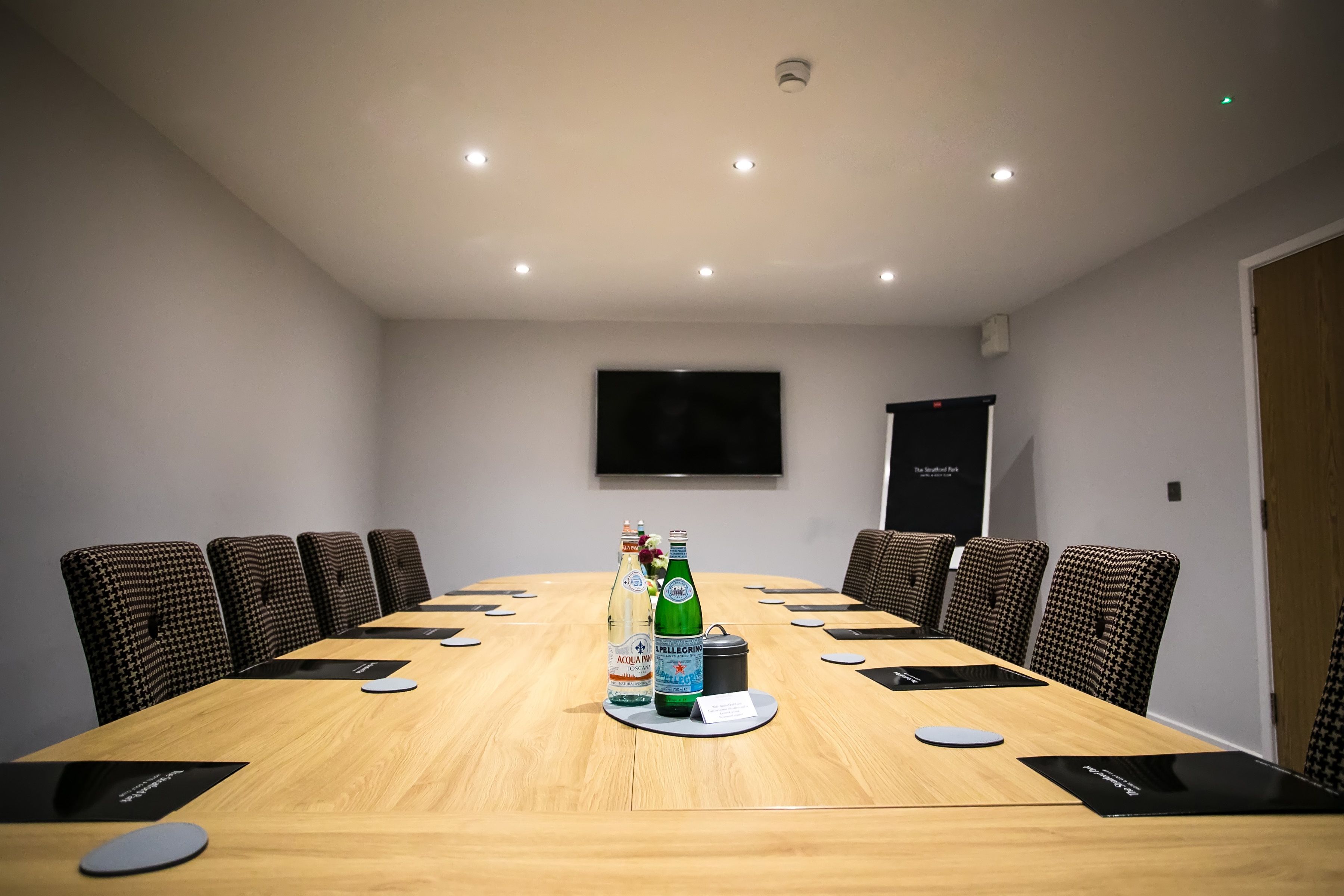 A conference room with a long table, chairs, a television on the wall, and a bottle of water and a bottle of beer on the table.