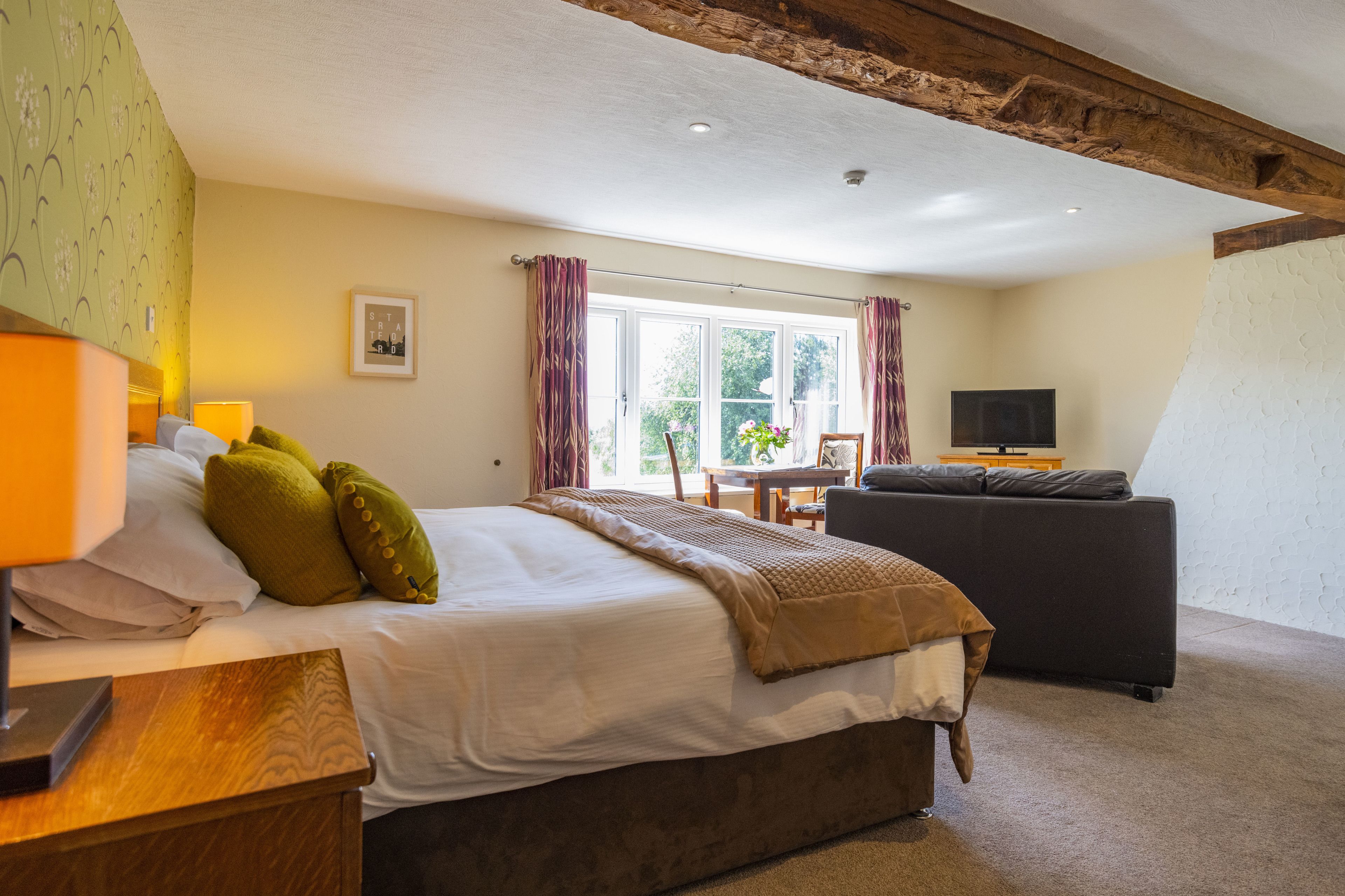 A bedroom with a bed, a wooden nightstand, a television, and a window with curtains.
