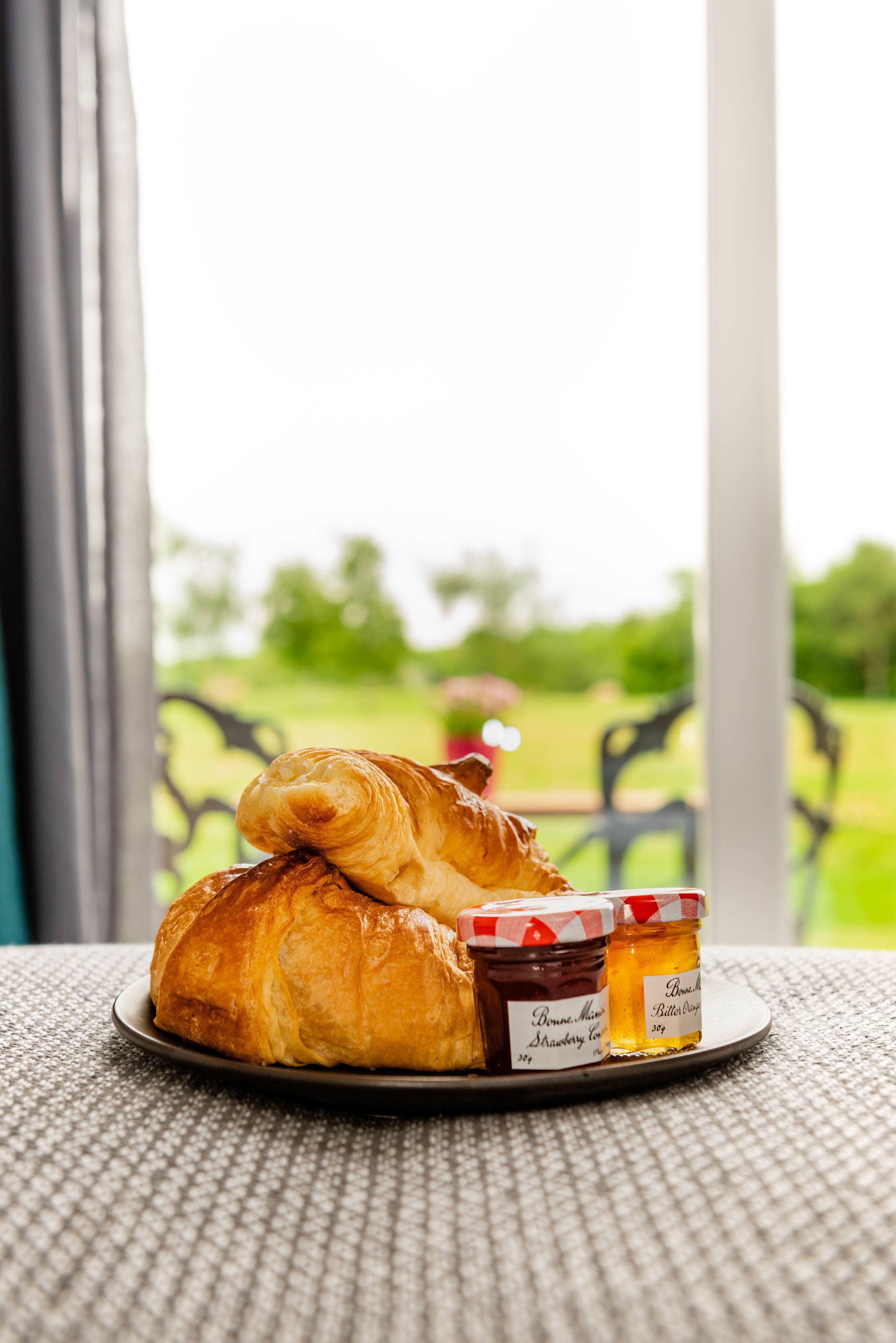 Un plato con croissants y frascos de mermelada sobre un mantel texturizado.