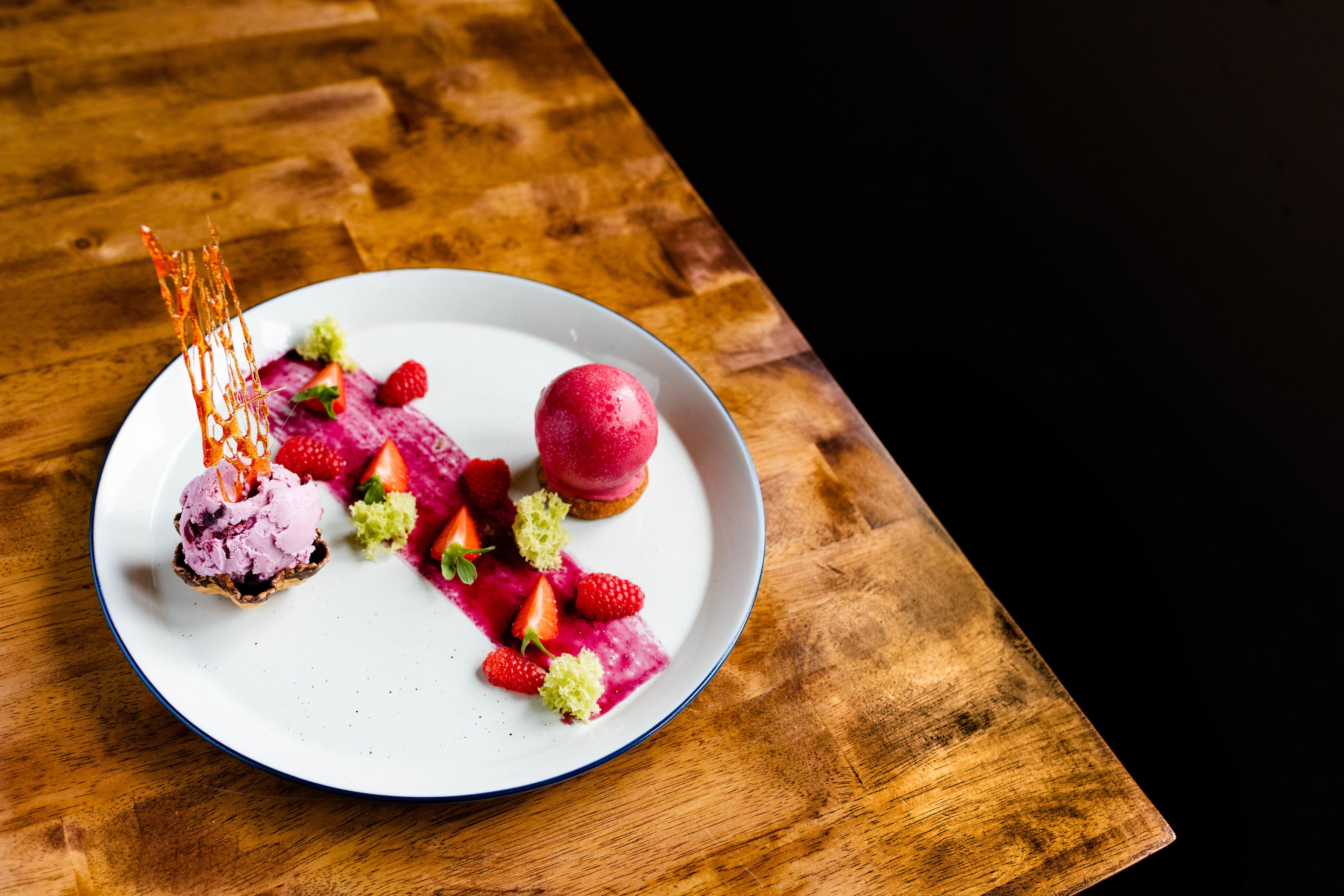 A dessert plate with various fruits and a scoop of ice cream on a white plate with a blue rim, placed on a wooden table.