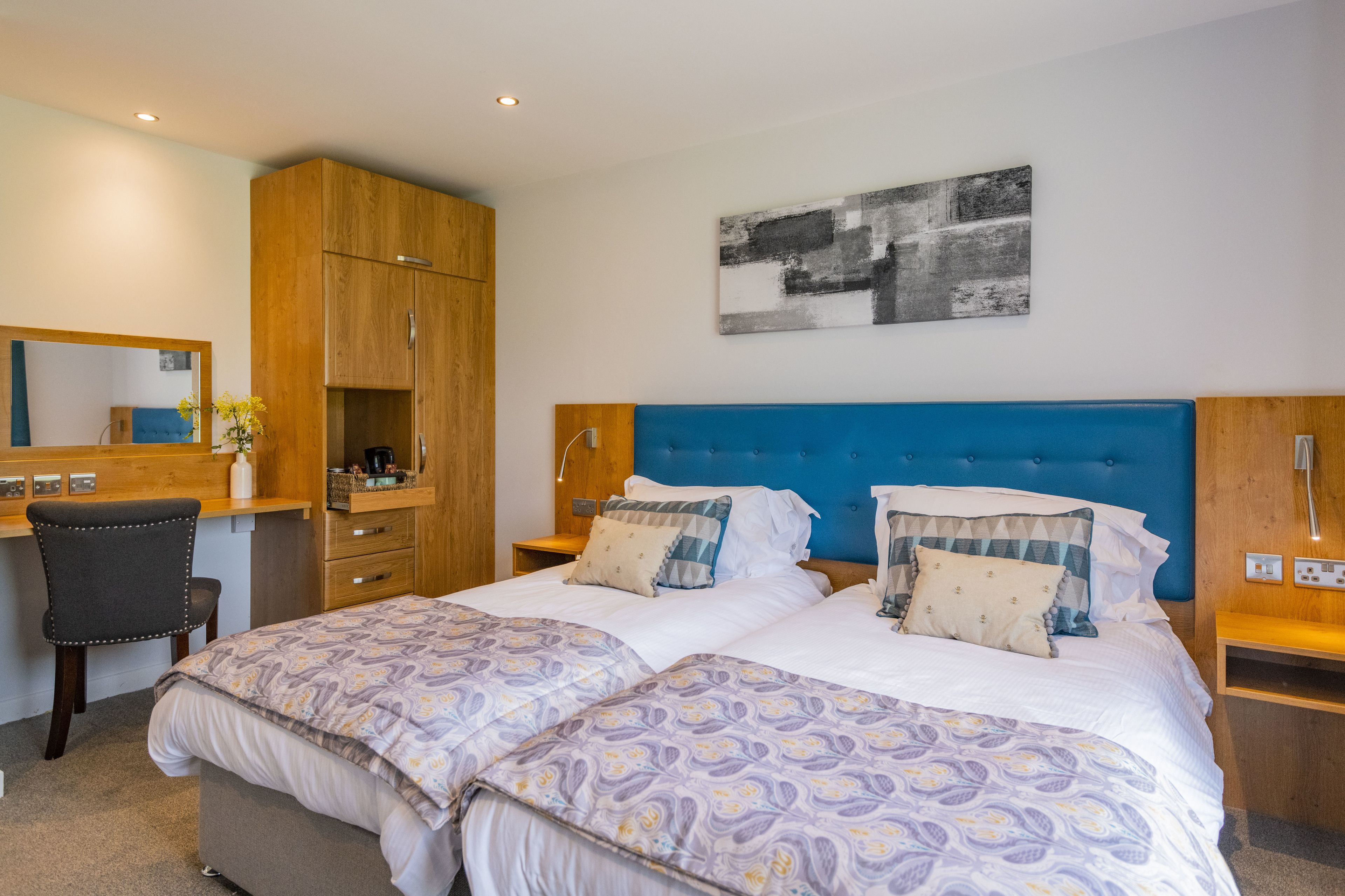 A hotel room with two beds, a desk, a chair, and a wardrobe.