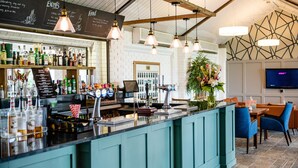A bar area with a teal counter, various bottles, and a menu board. - The Stratford Park Hotel & Golf Club (Stratford-upon-Avon)