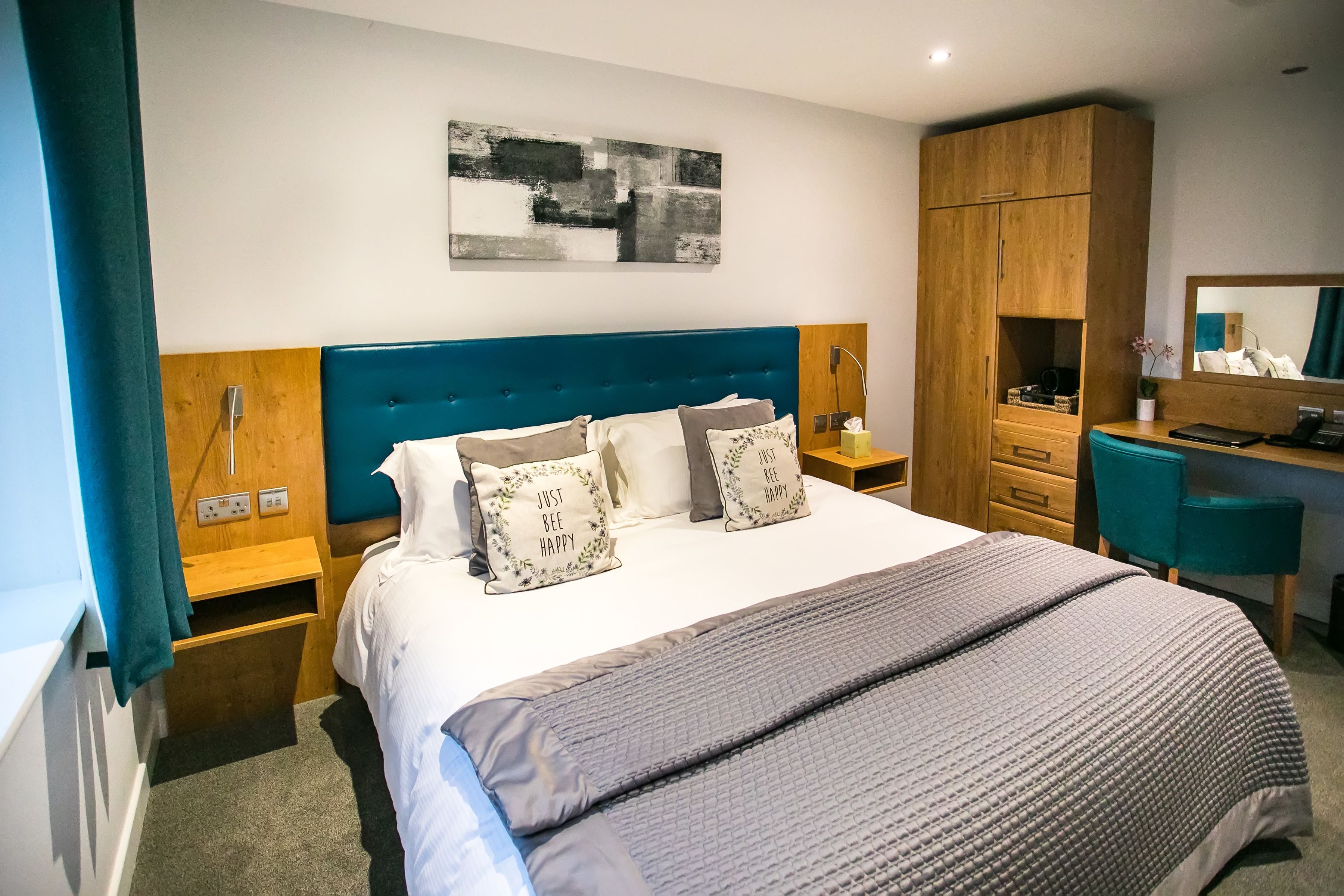 A hotel room with a large bed, a wooden wardrobe, a desk with a chair, and a mirror.