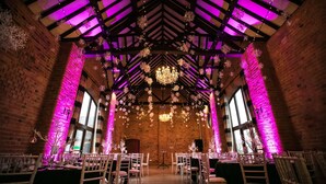 A venue with brick walls, wooden beams, and a high ceiling. Tables are set up for an event, with chairs arranged around them. - The Stratford Park Hotel & Golf Club (Stratford-upon-Avon)