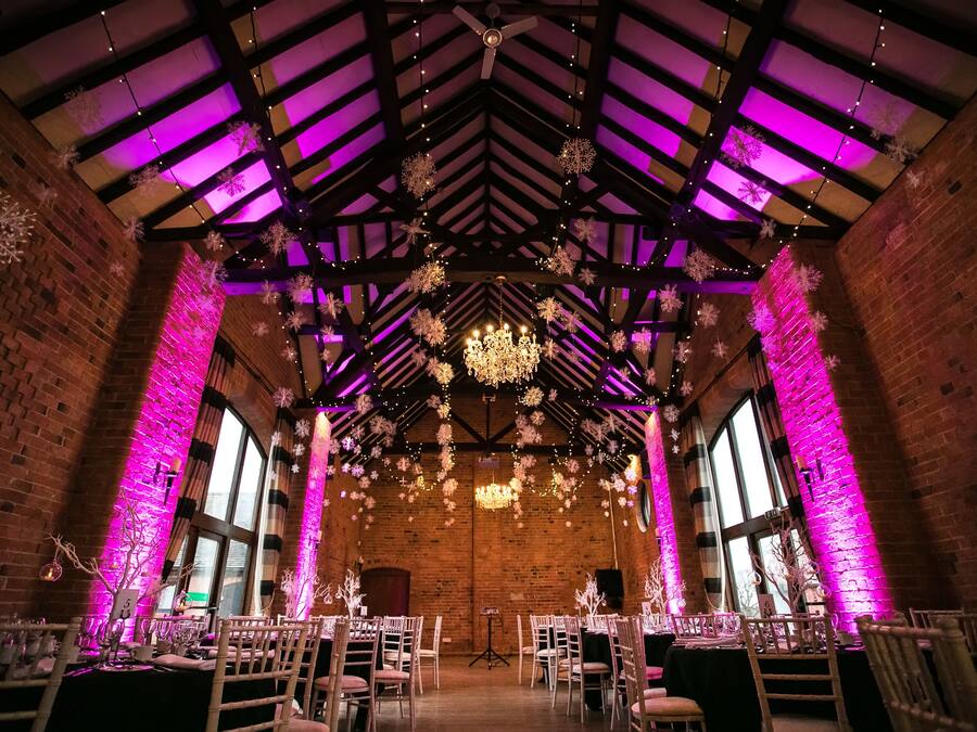 A venue with brick walls, wooden beams, and a high ceiling. Tables are set up for an event, with chairs arranged around them.